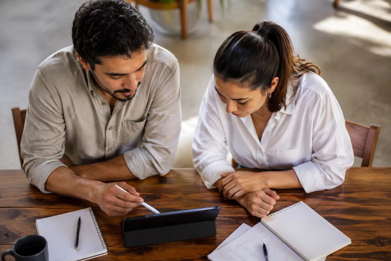Duas pessoas revisando anotações em um tablet sobre uma mesa de madeira